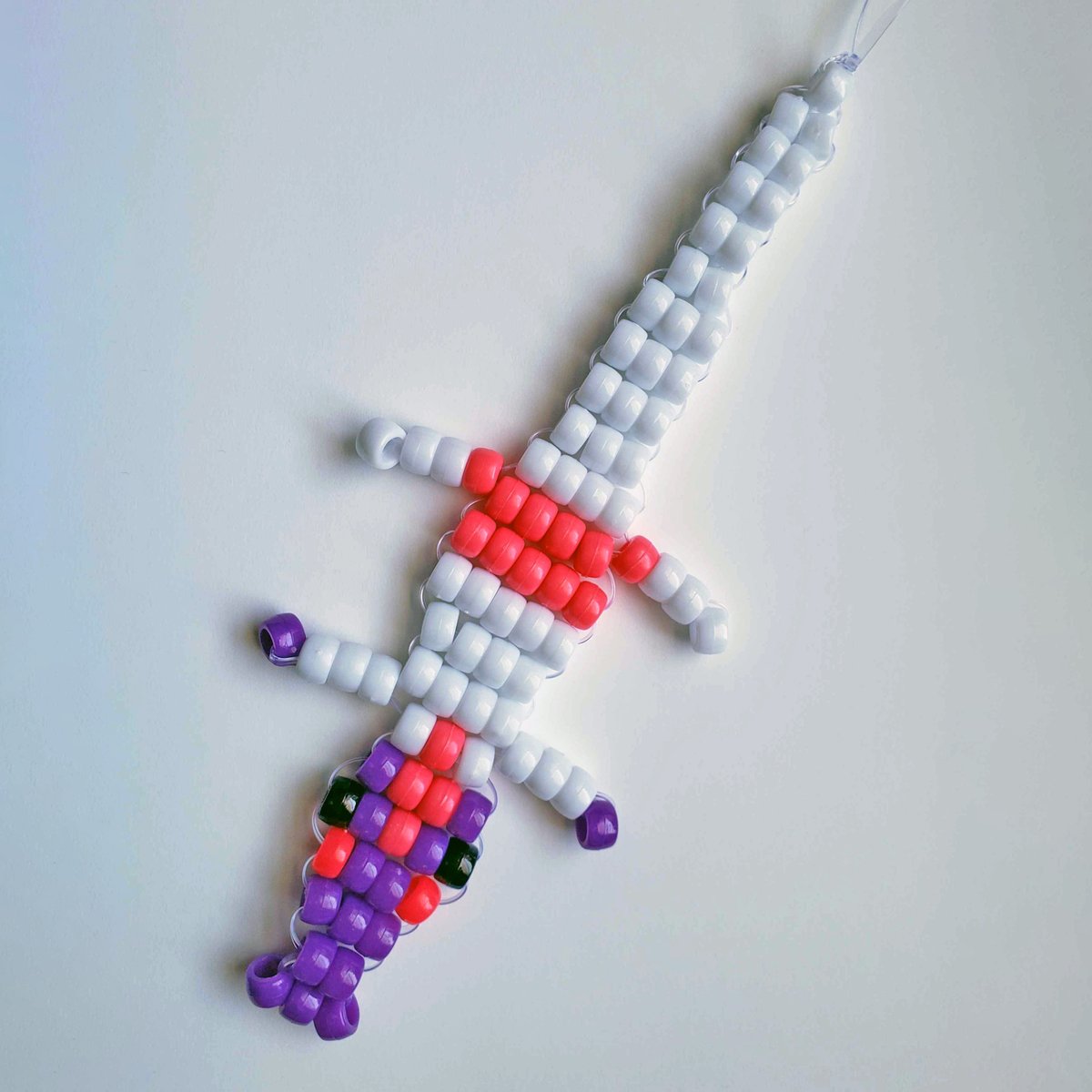 a beadwork crocodile figure. He's white with a purple face, pink hair, and pink shorts.