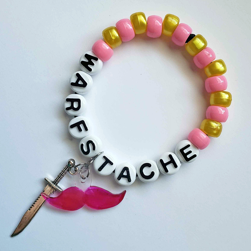 a pink and yellow bracelet that reads 'Warfstache;' from it hangs a pink mustache charm and a tiny knife charm.