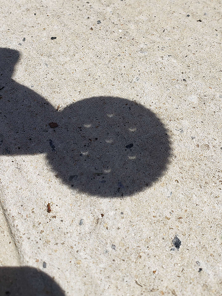 a shadow showing a person (me) holding out a Ritz cracker; each of the five holes in the Ritz cracker display a crescent shape instead of a circle, showing the ongoing eclipse.