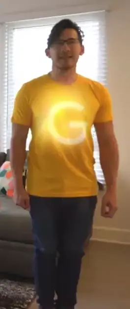 a man in a yellow shirt with a large glowing white 'G' on it, smiling; his image occasionally glitches